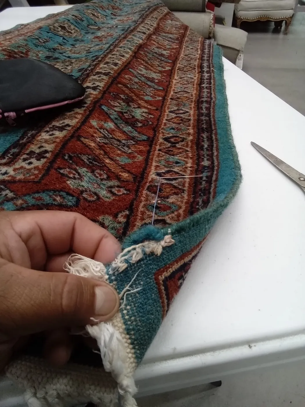Hands re-laying the fringe of a teal oriental rug at the repair bench